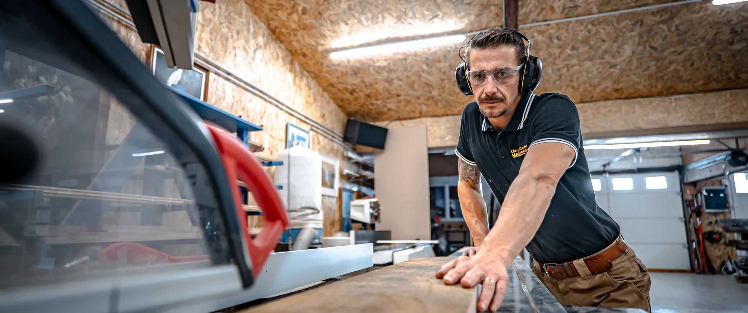Menuisier en protections auditives poussant une pièce de bois sur la scie de l’atelier