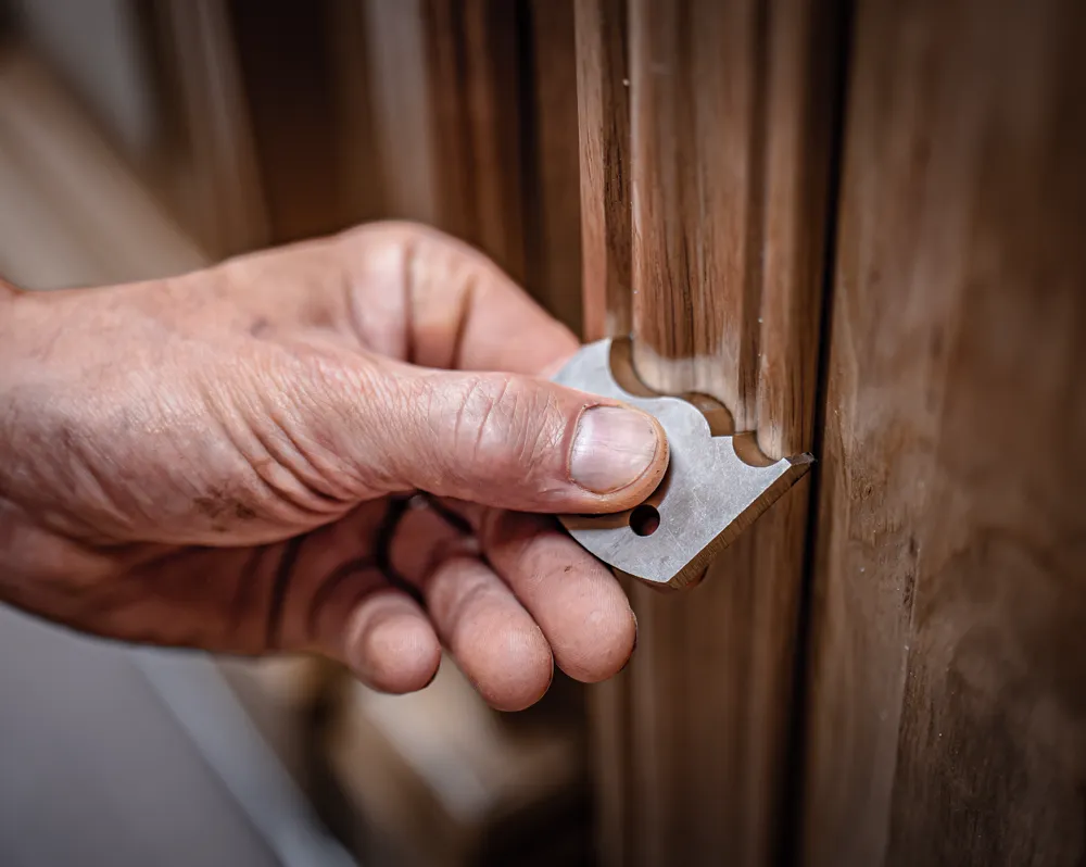 Main d’artisan présentant un gabarit métallique contre la moulure d’une porte ancienne