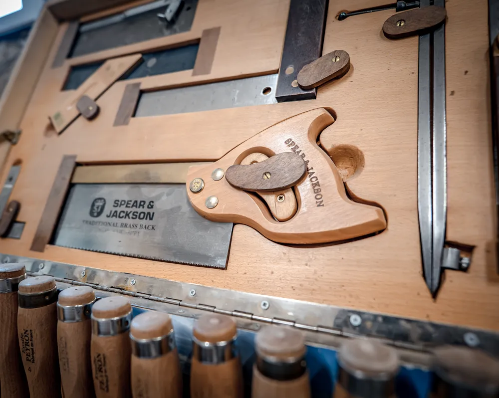 Scie à dos et rangée de ciseaux à bois sur le tableau d’outils de l’atelier
