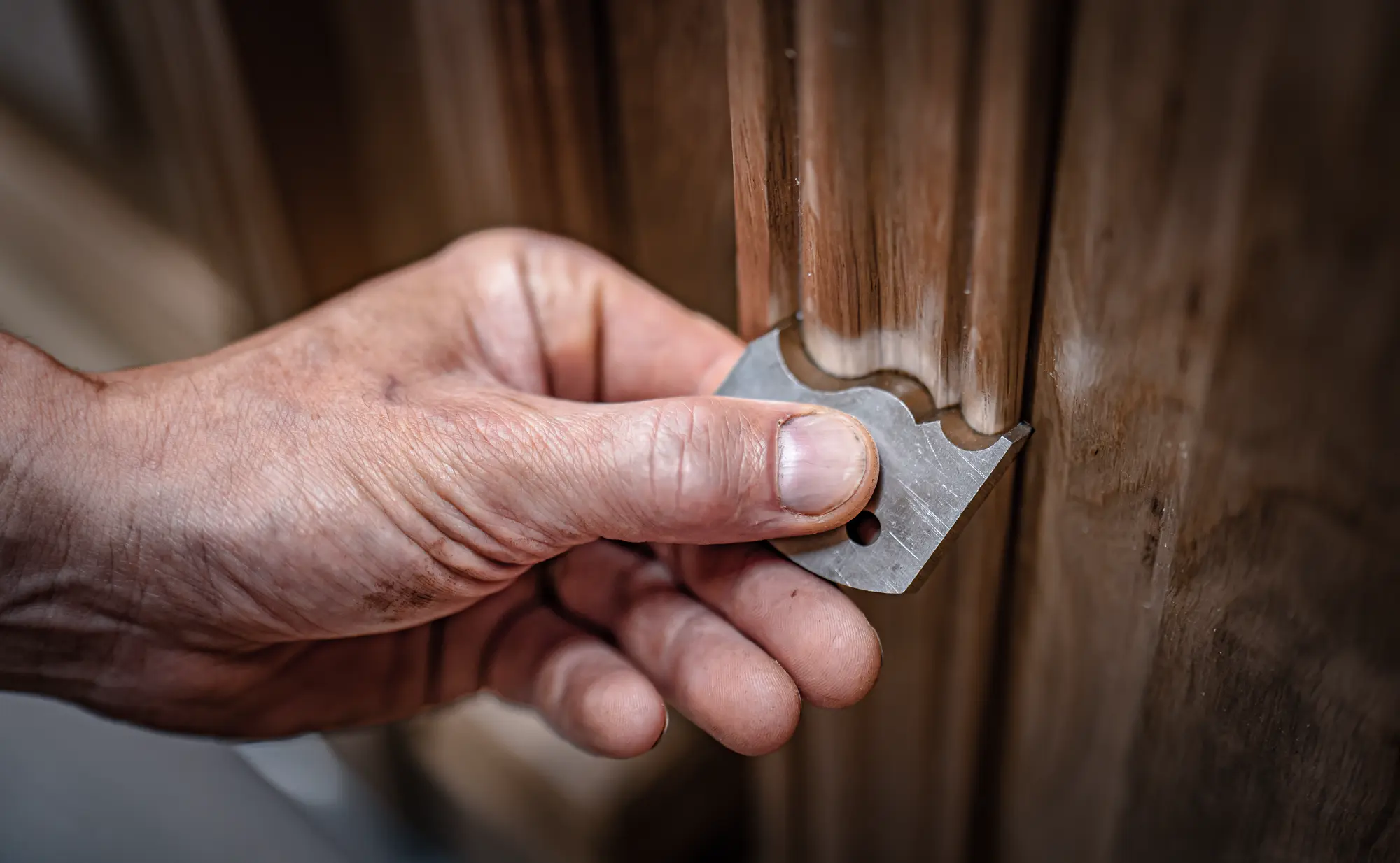 Main de l’artisan tenant un fer de rabot au-dessus d’un ouvrage bois