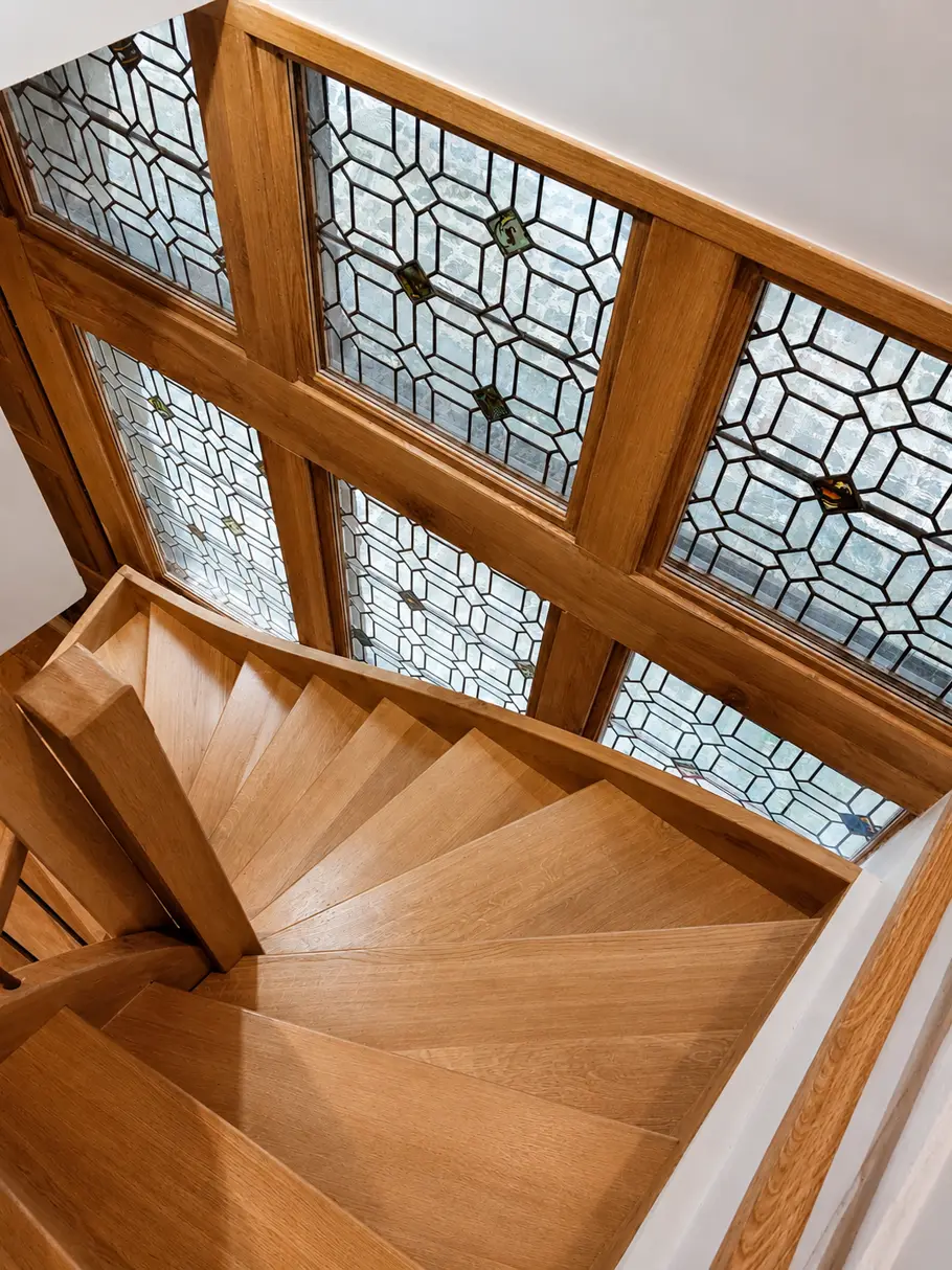 Escalier tournant en chêne devant des fenêtres à vitraux