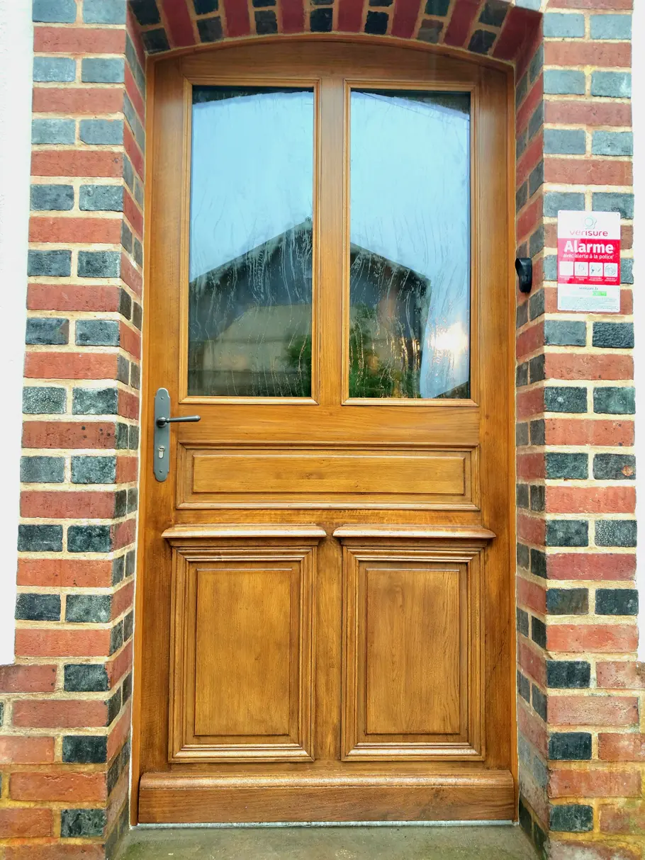 Porte d’entrée vitrée en chêne dans une façade de brique