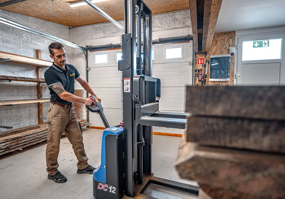 Menuisier déplaçant des plateaux de bois massif au gerbeur dans l’atelier